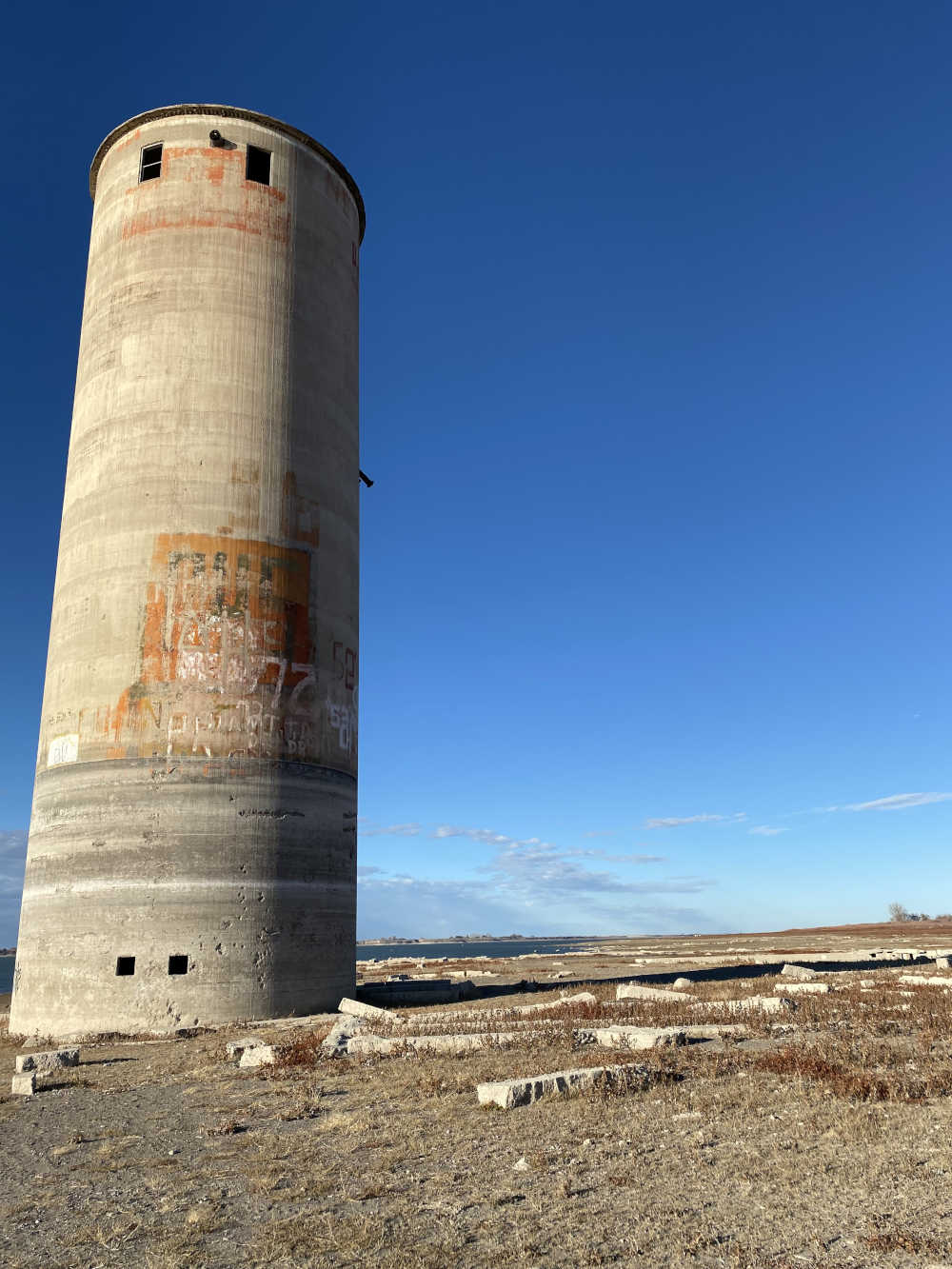In a field, an abandoned grain silo sits to the left of some structural foundations.